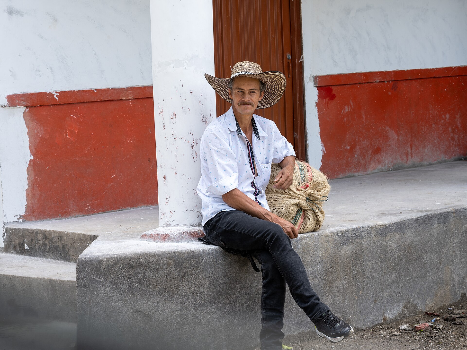 Caficultor colombiano sentado con un saco de café junto a una casa